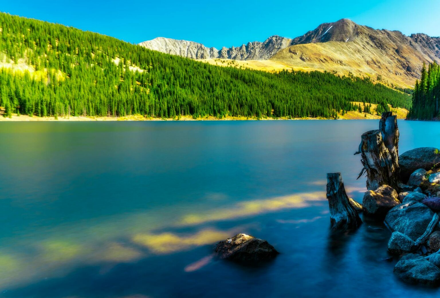 scenic view of the mountains with green pine trees beside calm body of water